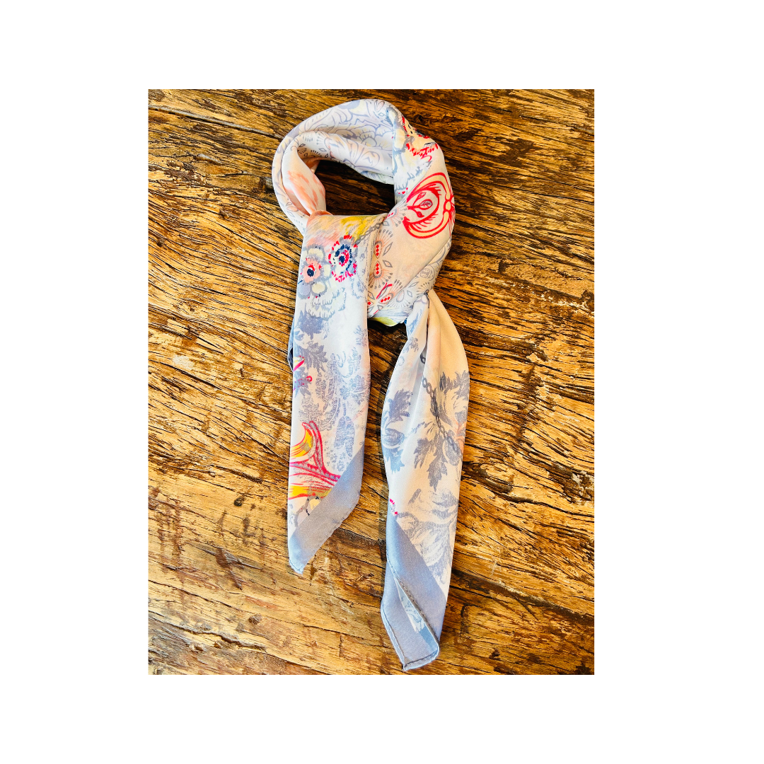 A lightweight square scarf with a light blue and white abstract print and colorful floral accents, styled on a rustic wooden surface.