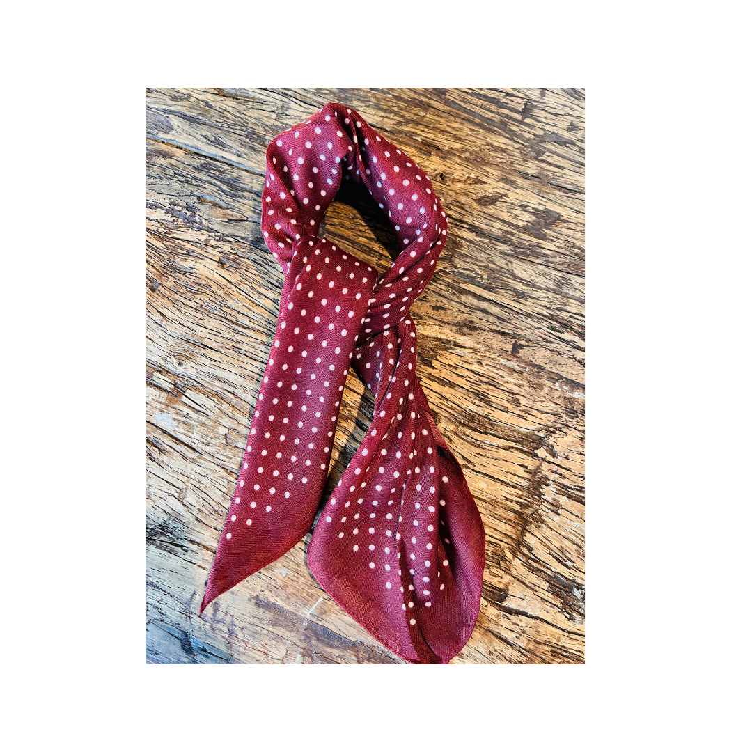 A burgundy scarf with a white polka-dot pattern, styled in a knot and draped over a rustic wooden surface.