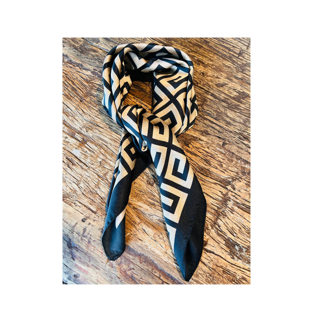 A black and beige geometric patterned scarf with a Greek key design, laid flat on a rustic wooden surface.
