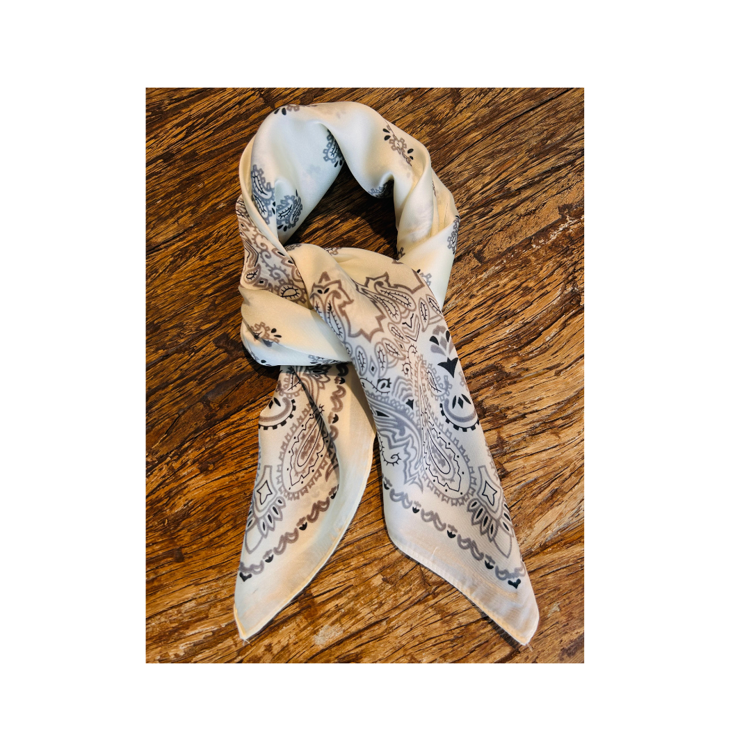 A cream-colored silk scarf with a black and gray paisley pattern, tied in a loop and displayed on a rustic wooden surface.