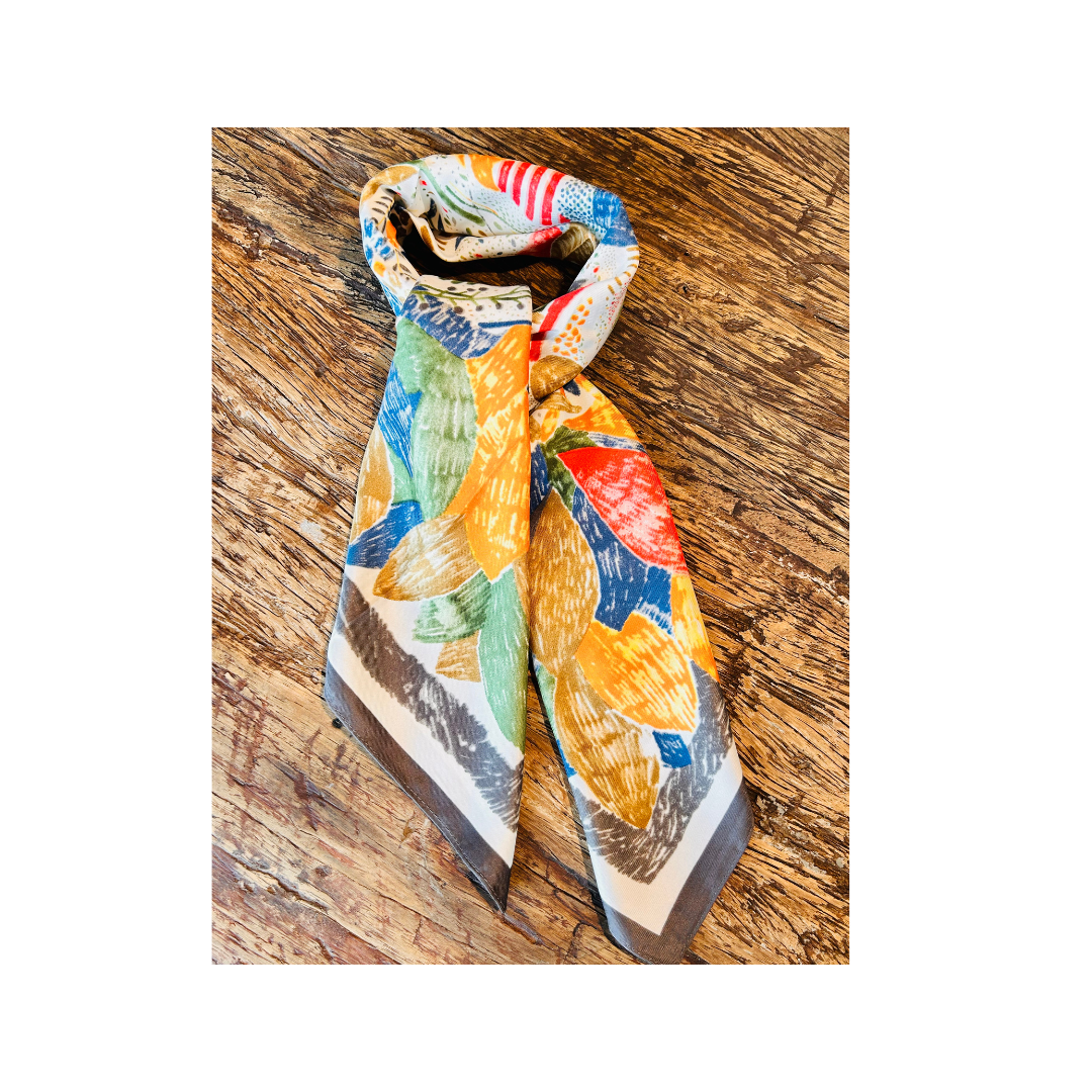 A multicolor scarf with a bold abstract pattern in yellow, blue, green, red, and gray, styled on a rustic wooden surface.