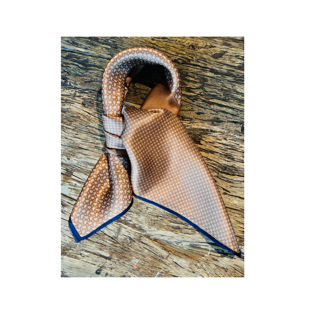 A patterned silk necktie in beige, brown, and white with a blue edge trim, tied in a knot and displayed on a rustic wooden surface.